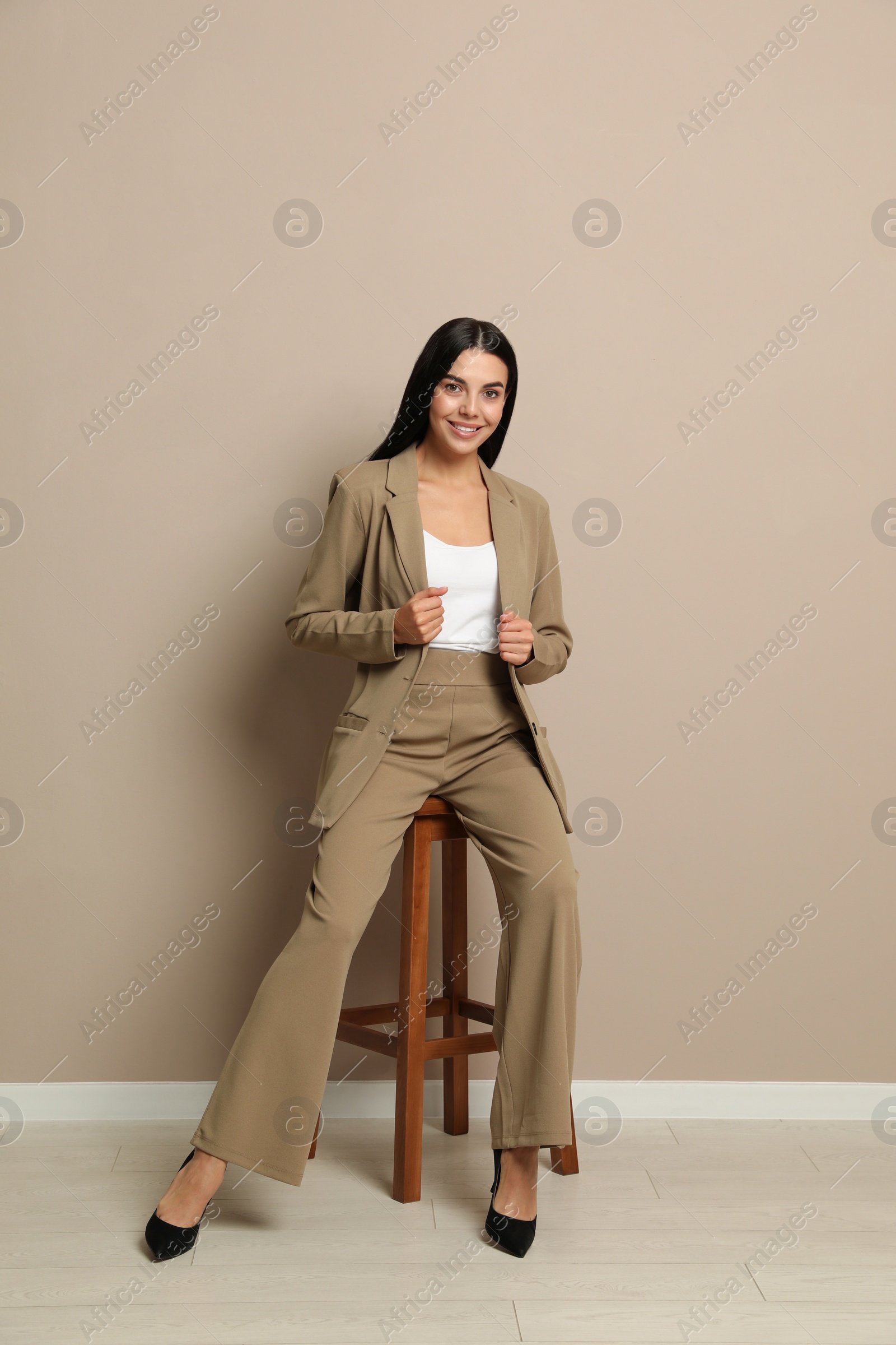 Photo of Beautiful young businesswoman sitting on stool near beige wall