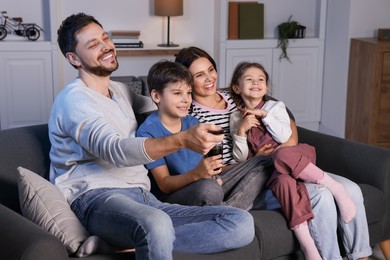 Happy family watching TV at home in evening. Father changing channels with remote control