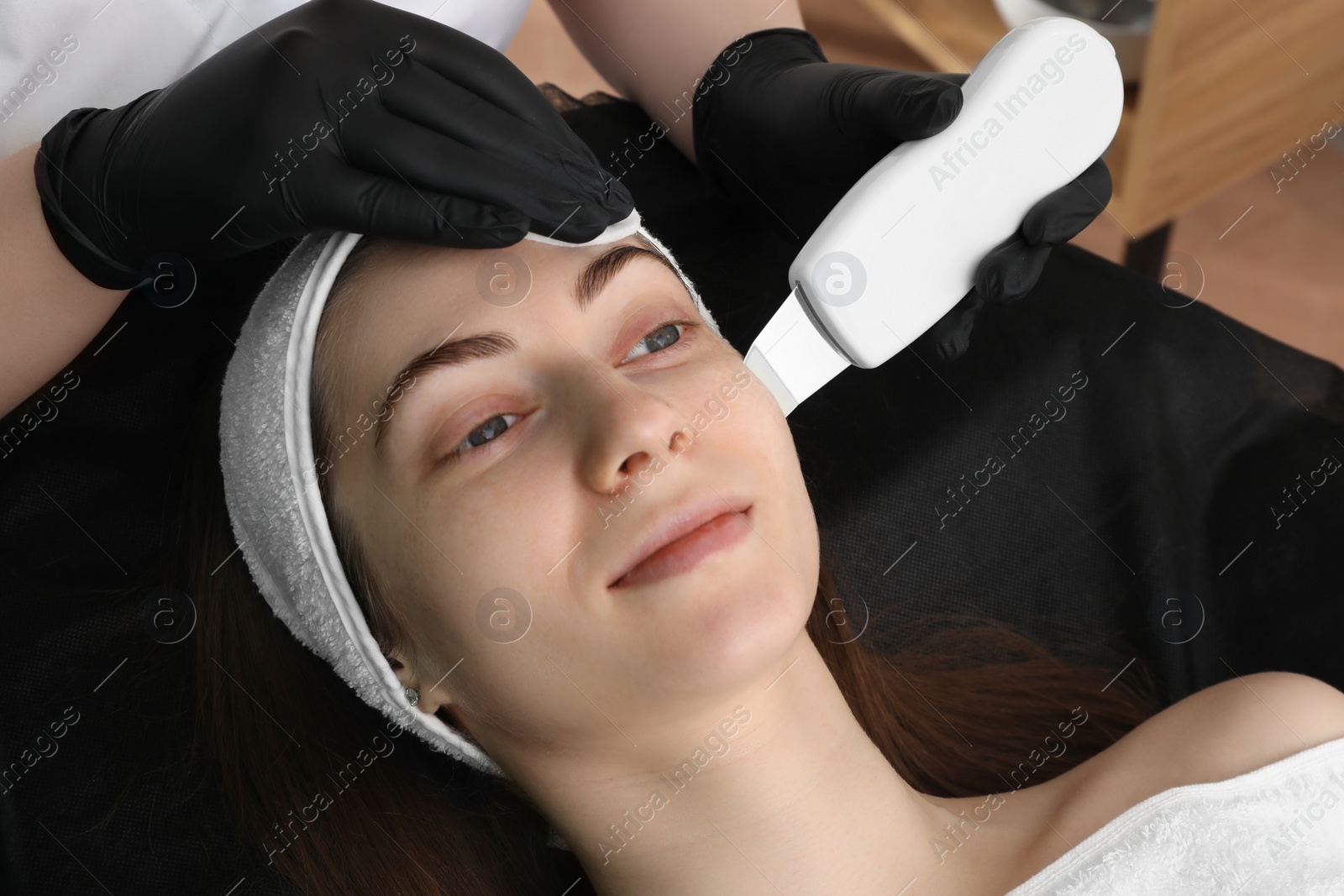 Photo of Cosmetologist using ultrasonic scrubber, closeup. Client having cleansing procedure indoors