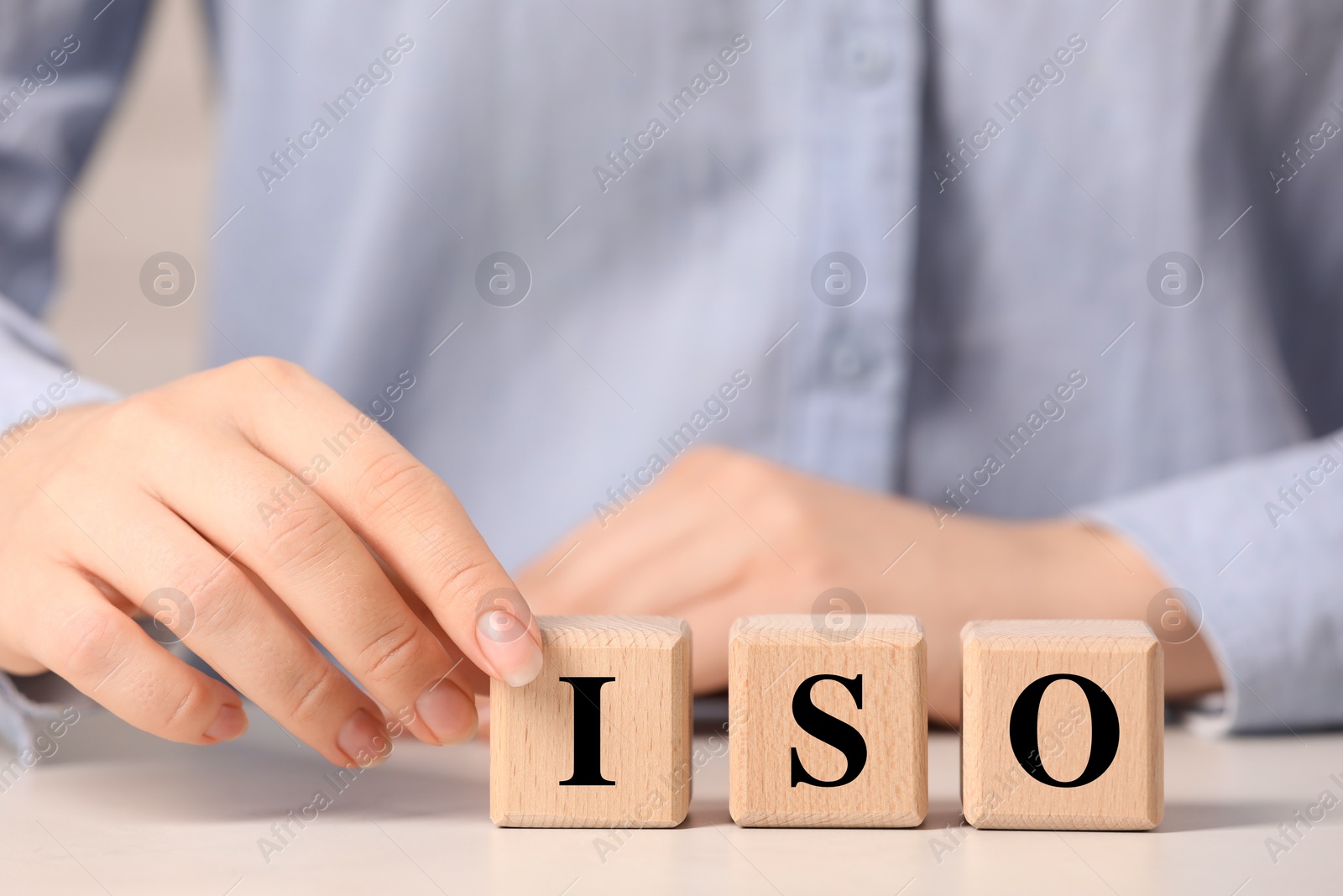 Photo of Woman making abbreviation ISO of wooden cubes at white table, closeup