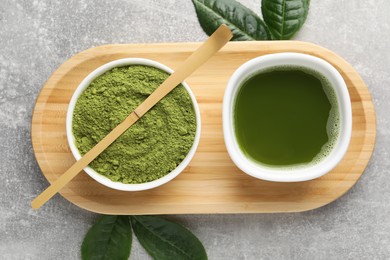 Photo of Green matcha powder, bamboo scoop, fresh beverage and leaves on light grey table, flat lay