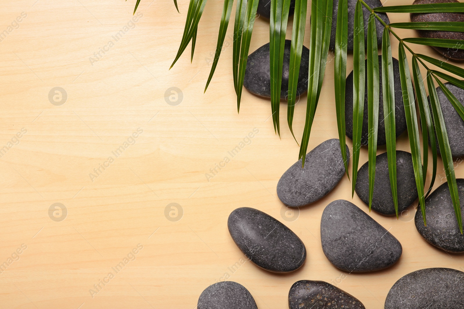 Photo of Spa stones with palm leaf on wooden background, top view. Space for text