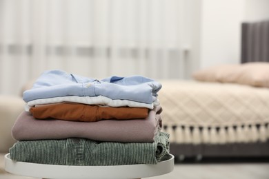 Photo of Stack of different folded clothes on side table indoors, closeup. Space for text