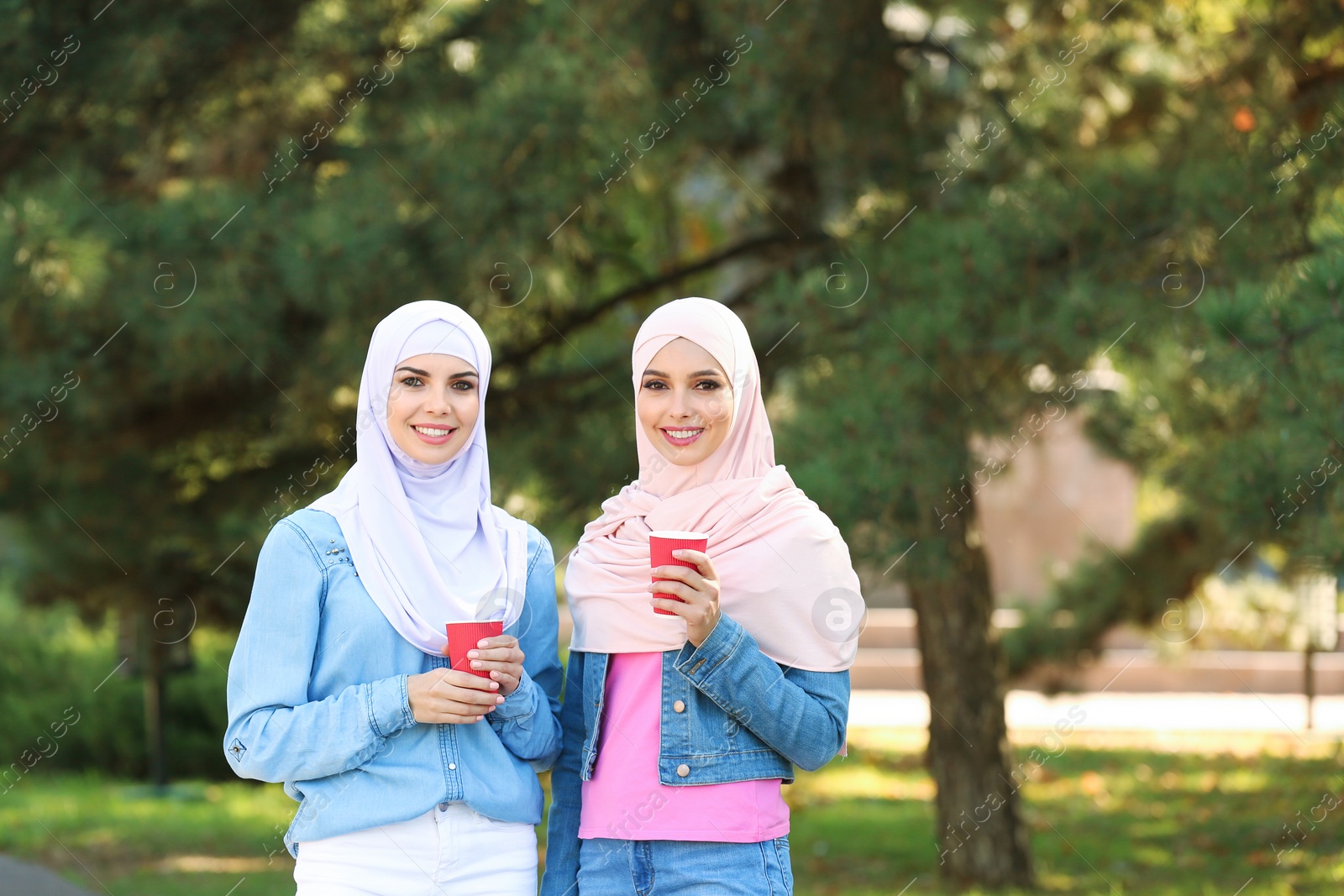 Photo of Muslim women with cups of coffee walking in park