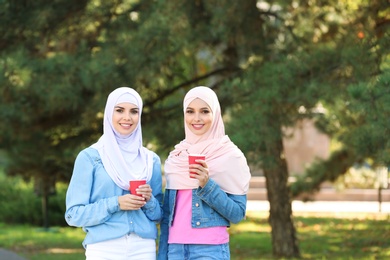 Muslim women with cups of coffee walking in park