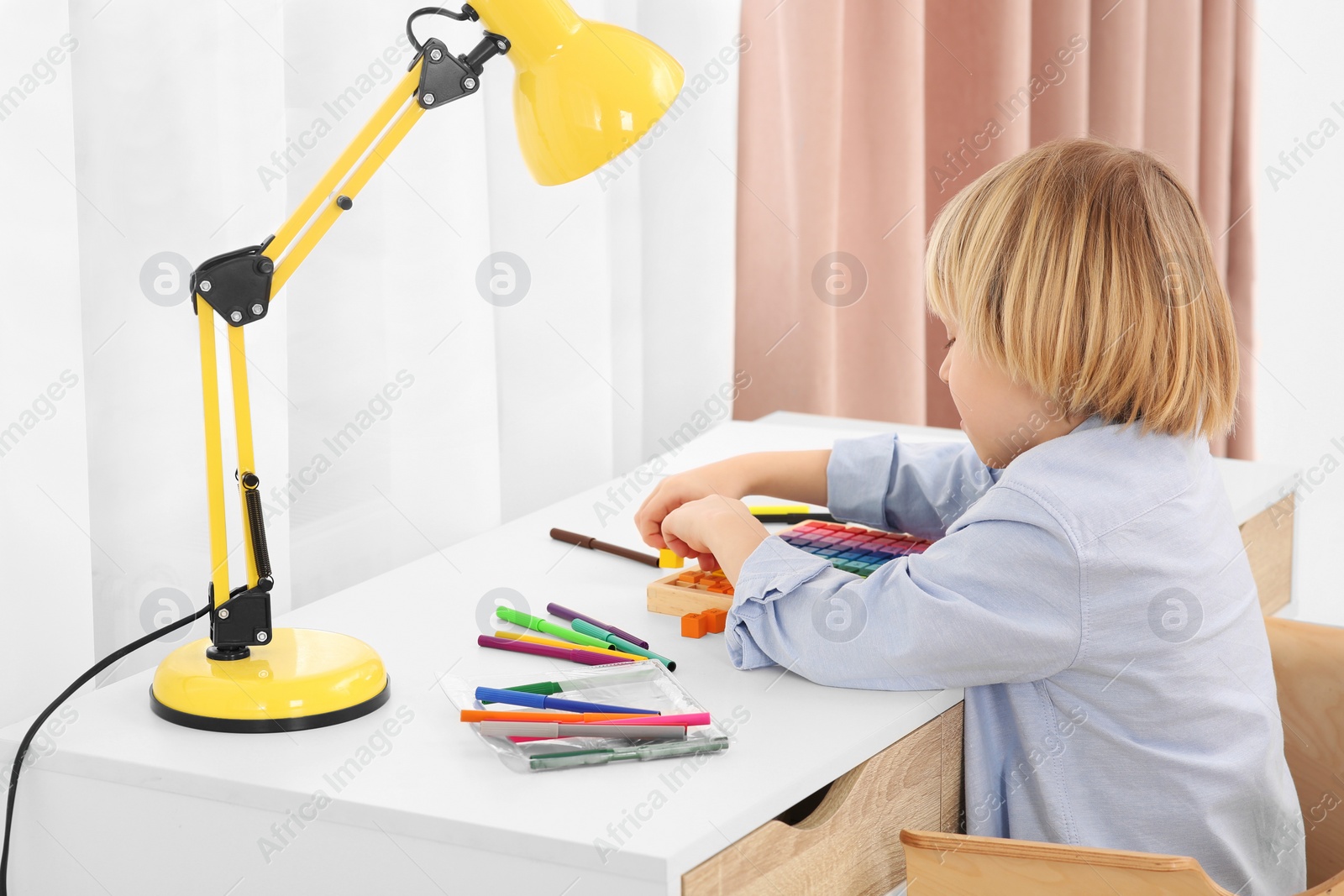 Photo of Cute little boy playing with colorful wooden cubes at desk in room. Home workplace
