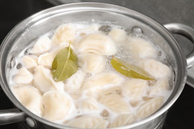 Photo of Cooking dumplings (varenyky) with tasty filling and bay leaves in pot indoors, closeup