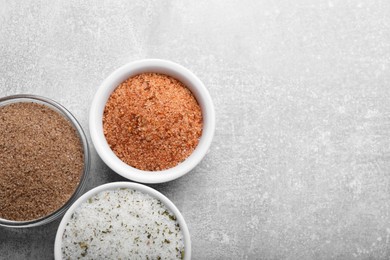 Different kinds of salt on grey table, flat lay. Space for text