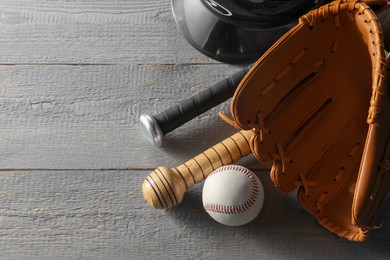 Photo of Baseball glove, bats and ball on grey wooden table, closeup. Space for text