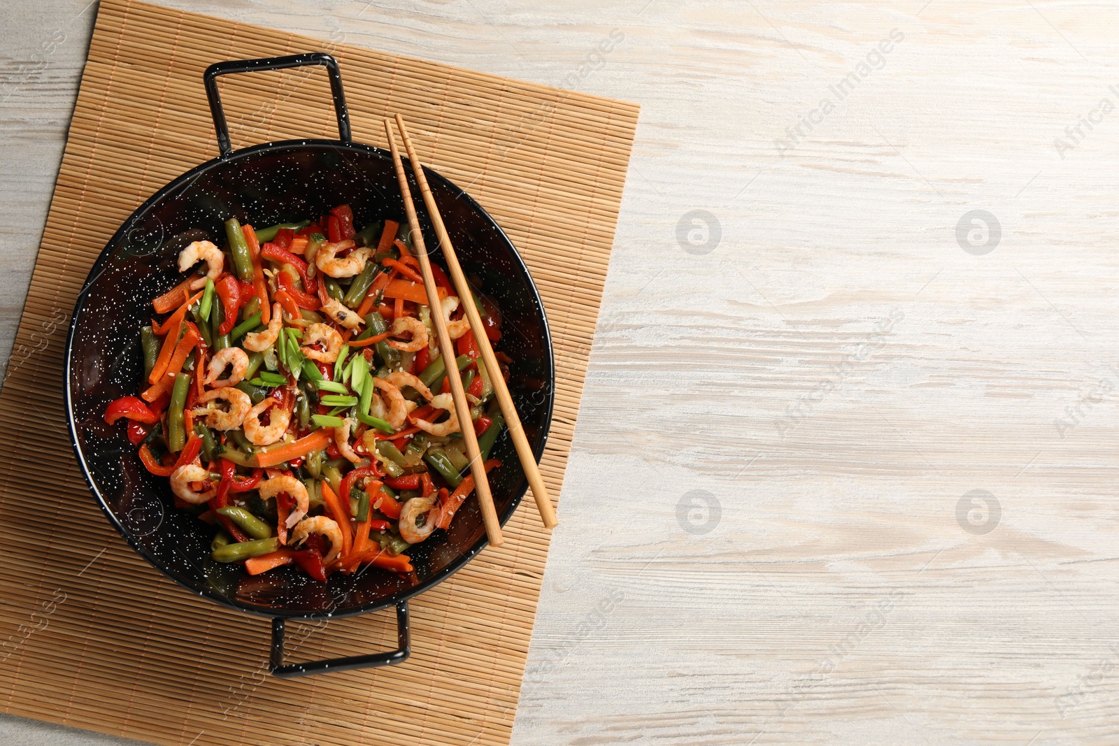 Photo of Shrimp stir fry with vegetables in wok and chopsticks on wooden table, top view. Space for text