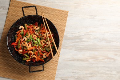 Shrimp stir fry with vegetables in wok and chopsticks on wooden table, top view. Space for text