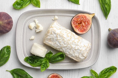 Photo of Delicious goat cheese with figs and basil on white wooden table, flat lay