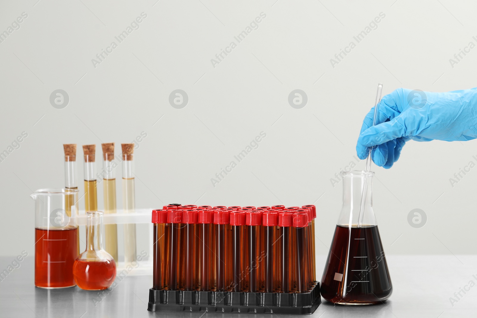 Photo of Scientist mixing brown liquid in conical flask against light background, closeup