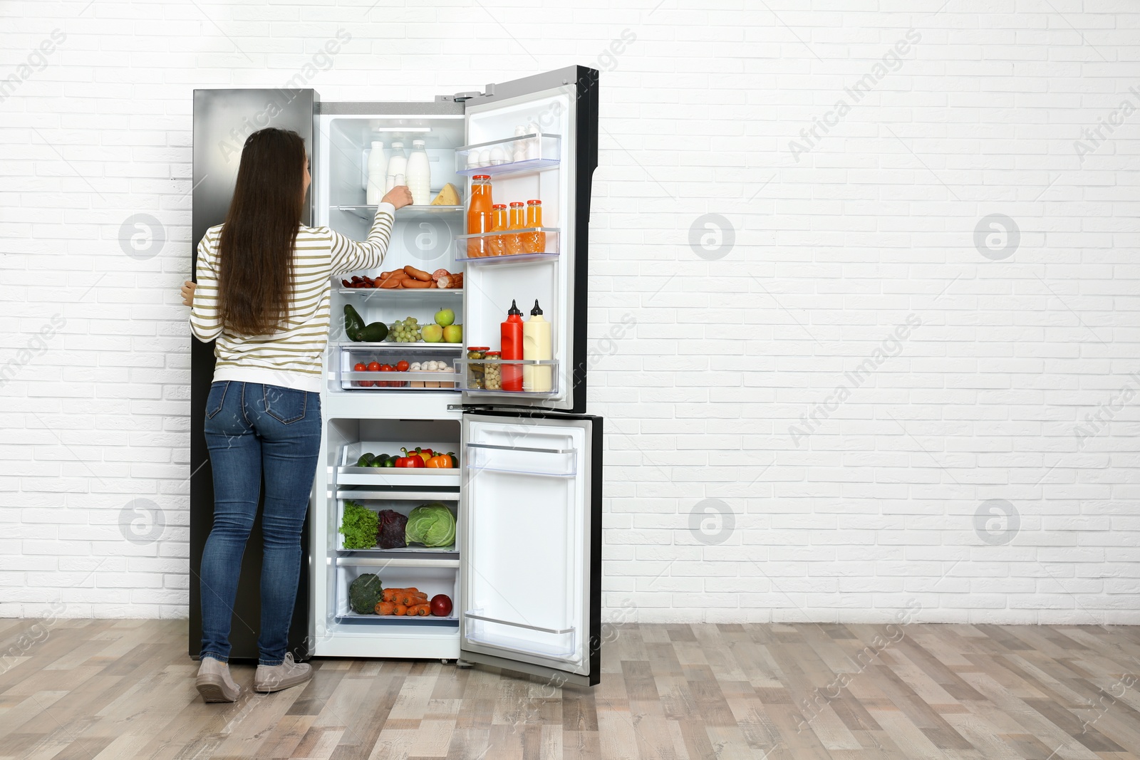 Photo of Young woman taking yoghurt out of refrigerator indoors, space for text