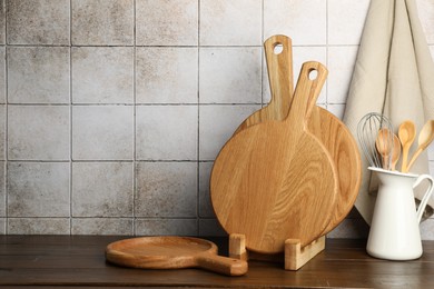 Wooden cutting boards and kitchen utensils on table near tiled wall. Space for text