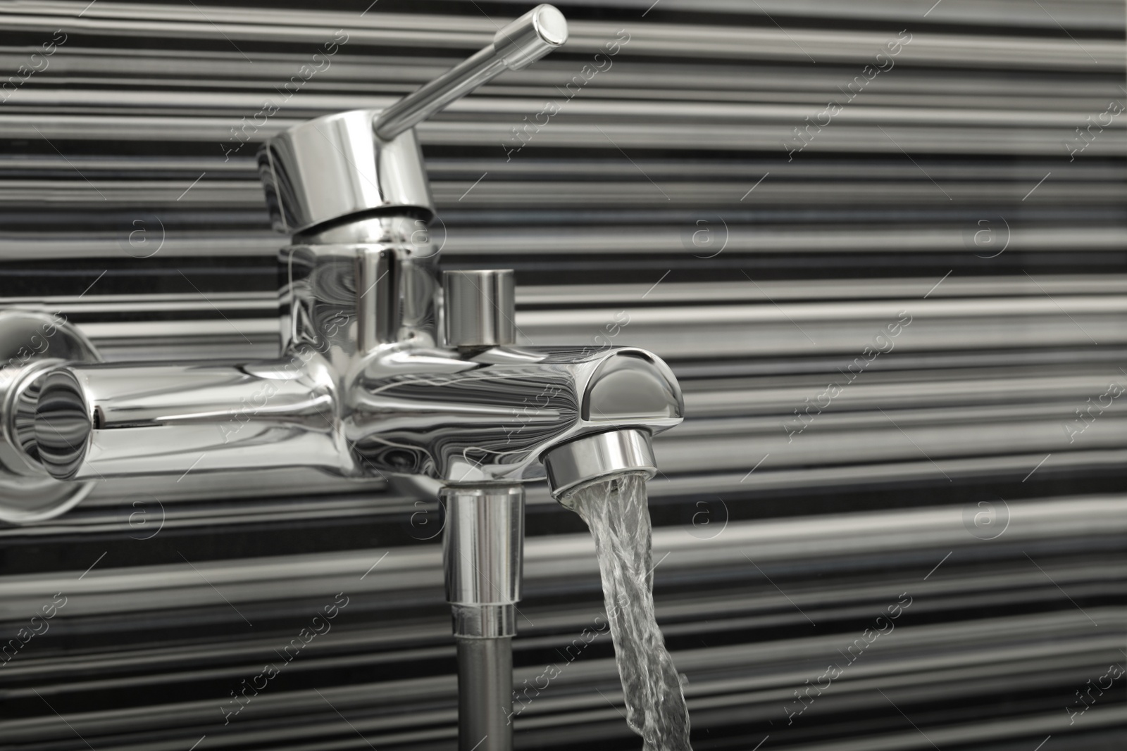 Photo of Water flowing from bath tap installed on black and white wall