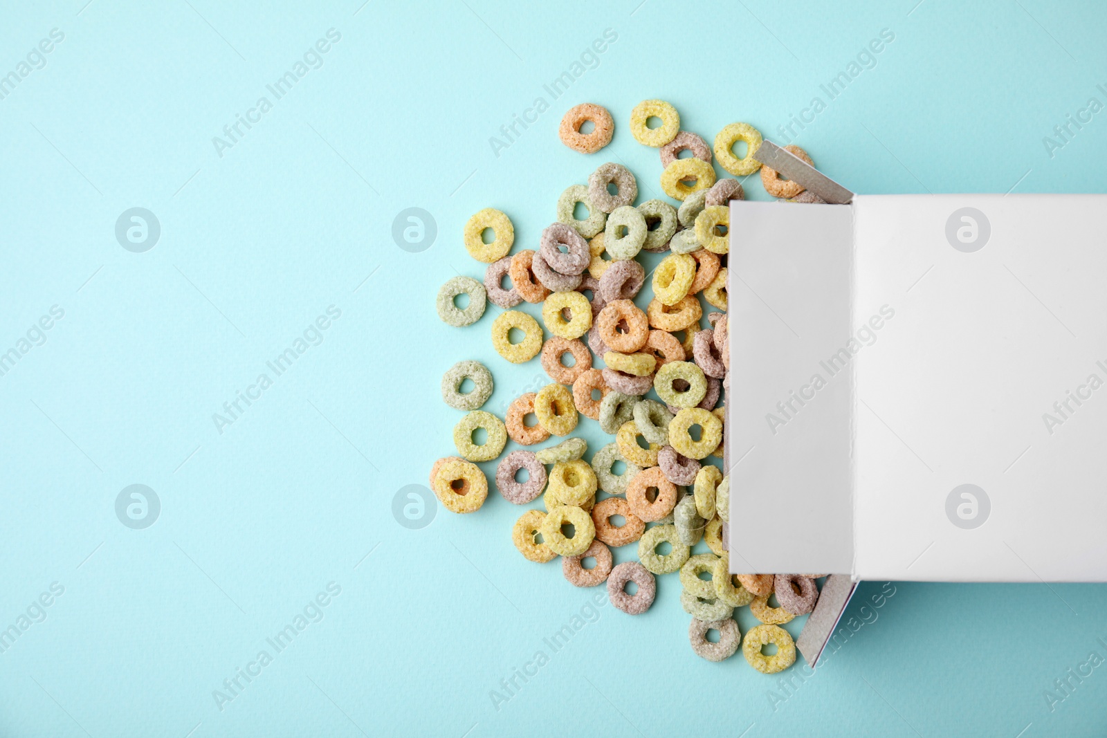 Photo of Paper box with tasty cereal rings on light blue background, flat lay. Space for text