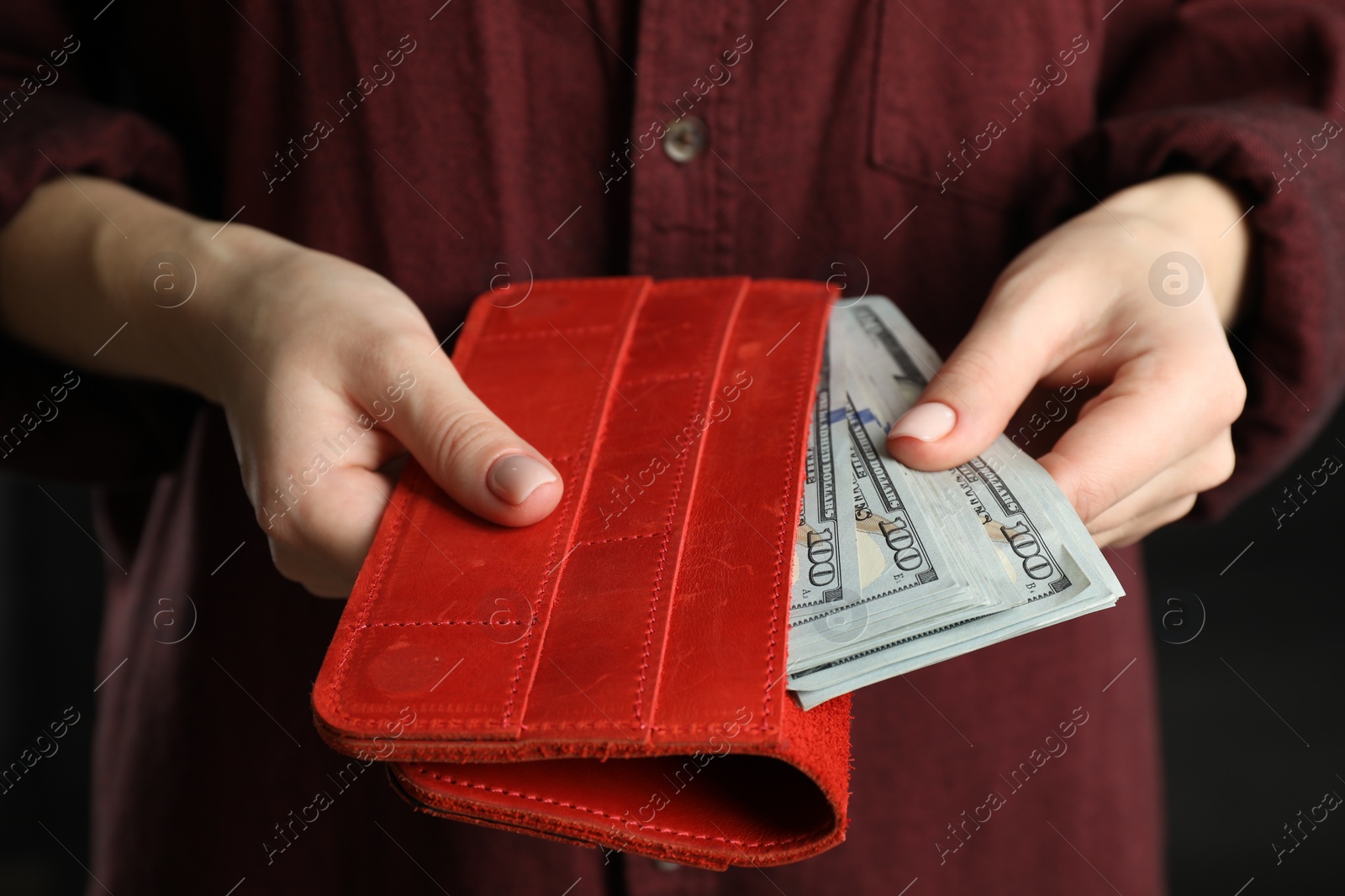 Photo of Money exchange. Woman putting dollar banknotes into wallet on dark background, closeup