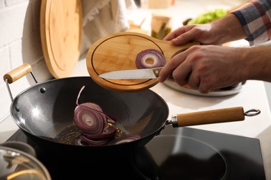 Photo of Man pouring onion slices into frying pan, closeup