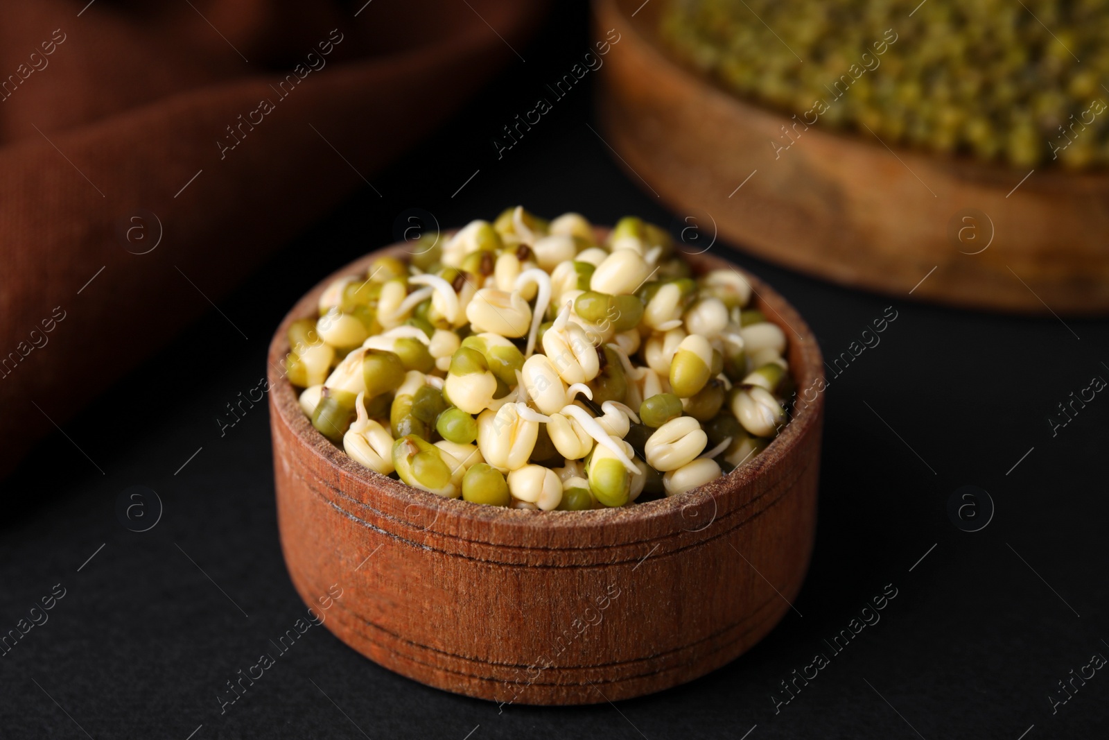 Photo of Wooden bowl with sprouted green mung beans on black background, closeup