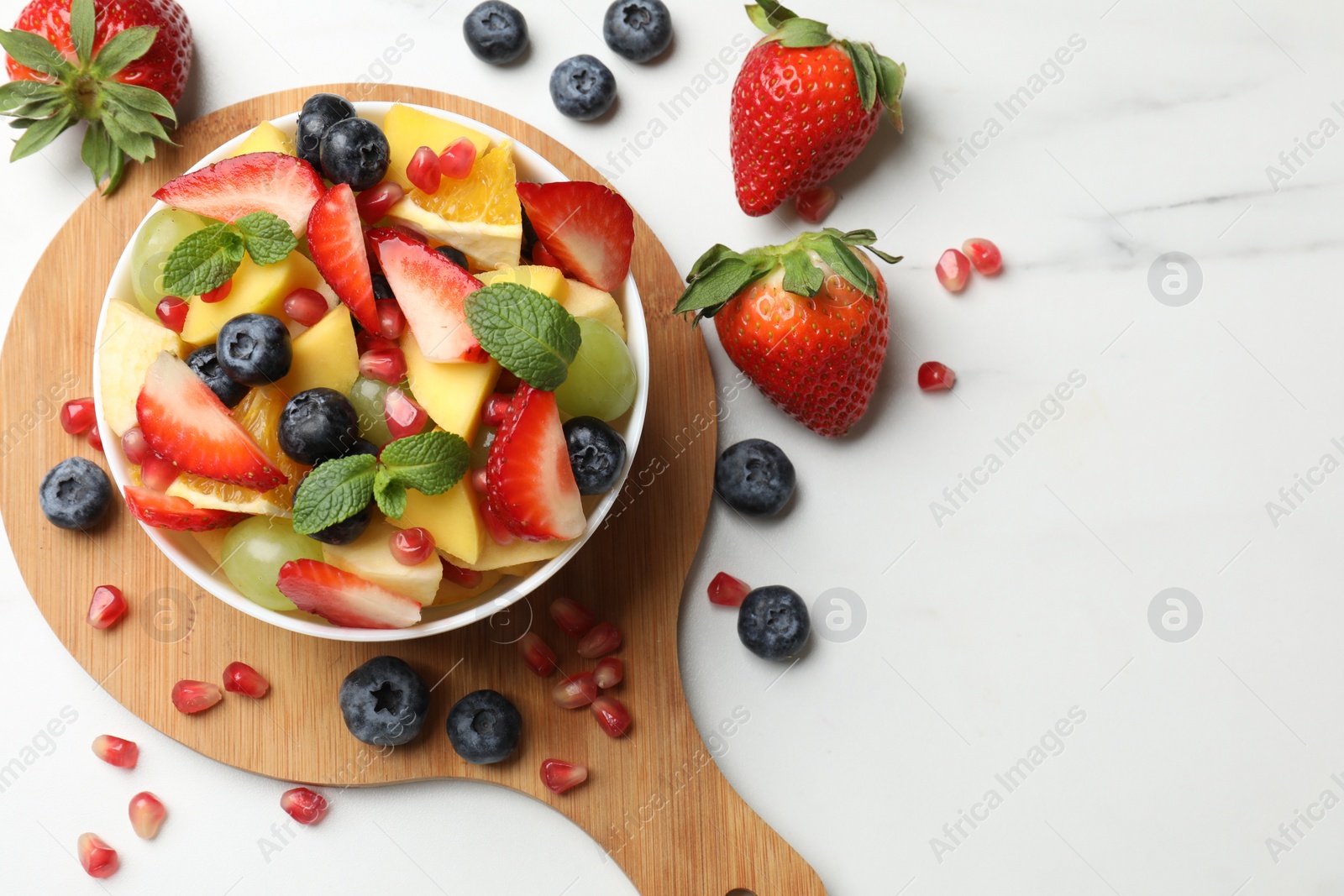 Photo of Tasty fruit salad in bowl and ingredients on white table, flat lay. Space for text