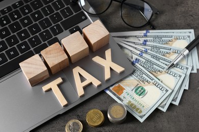 Photo of Word Tax made of wooden letters, cubes, laptop, banknotes and coins on grey table