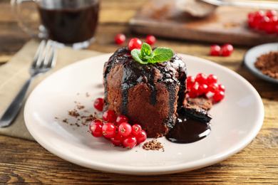 Photo of Delicious warm chocolate lava cake with mint and berries on wooden table, closeup