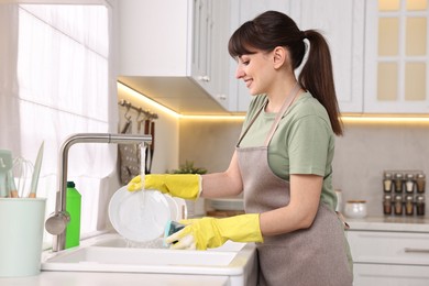 Photo of Happy young housewife washing dishes in kitchen sink. Cleaning chores