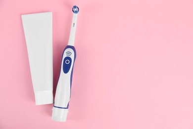 Electric toothbrush and toothpaste on pink background, flat lay. Space for text