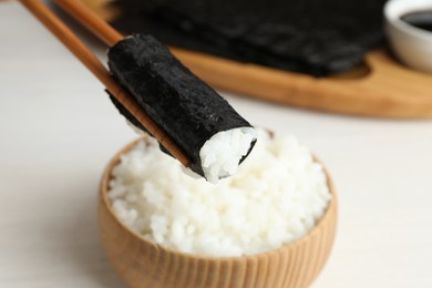 Chopsticks with cooked rice wrapped in nori sheet over white table, closeup