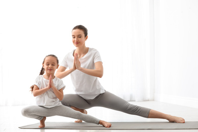 Photo of Young mother with little daughter practicing yoga at home