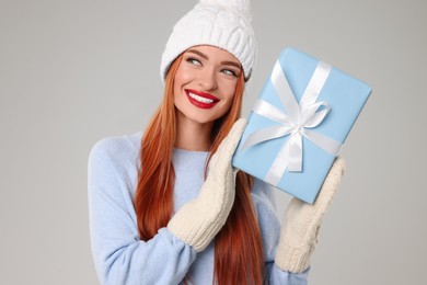 Photo of Young woman in hat and sweater with Christmas gift on light grey background