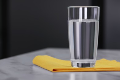 Photo of Glass of water and napkin on white table against blurred background. Space for text