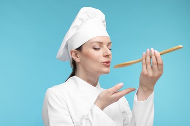 Photo of Woman chef in uniform tasting something on light blue background