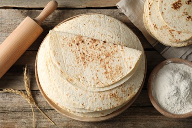 Photo of Tasty homemade tortillas, flour, rolling pin and spikes on wooden table, flat lay