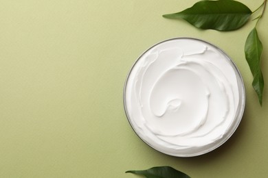 Photo of Jar of face cream and fresh leaves on light green background, flat lay. Space for text