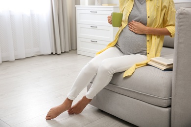 Beautiful pregnant woman drinking tea at home, closeup