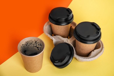 Photo of Takeaway paper coffee cups with plastic lids and cardboard holder on color background