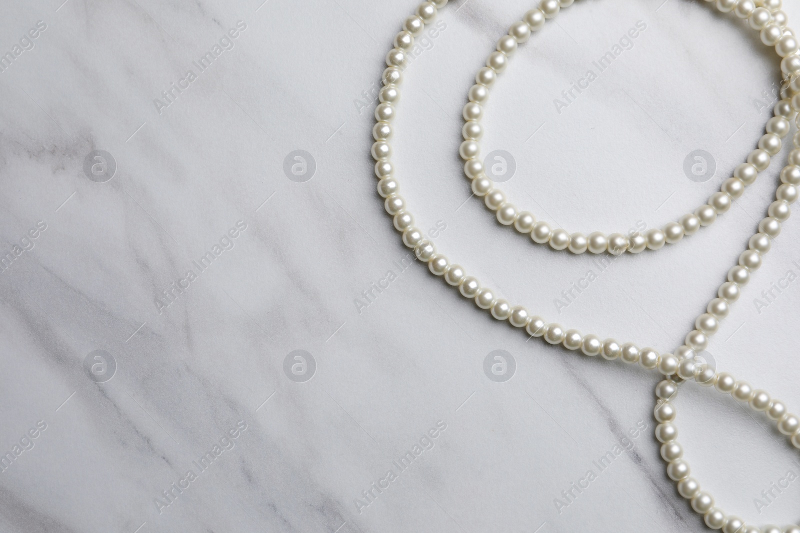 Photo of Elegant pearl necklace on white marble table, top view. Space for text