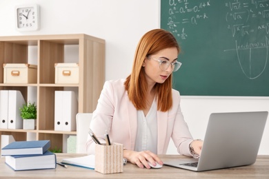 Beautiful young teacher with laptop sitting at table in classroom