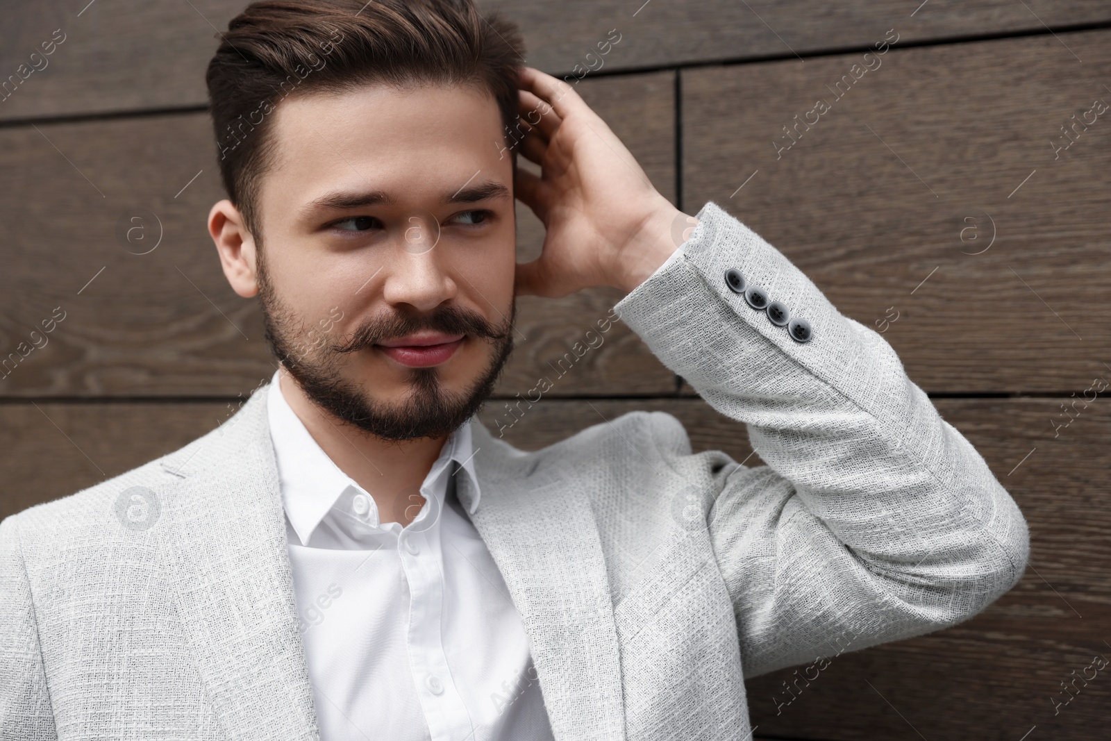 Photo of Smiling man in white suit touching his head near brown brick wall