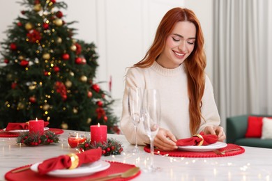 Beautiful young woman setting table in room decorated for Christmas