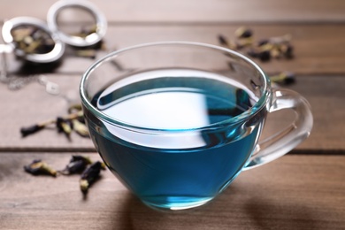 Glass cup of organic blue Anchan on wooden table, closeup. Herbal tea