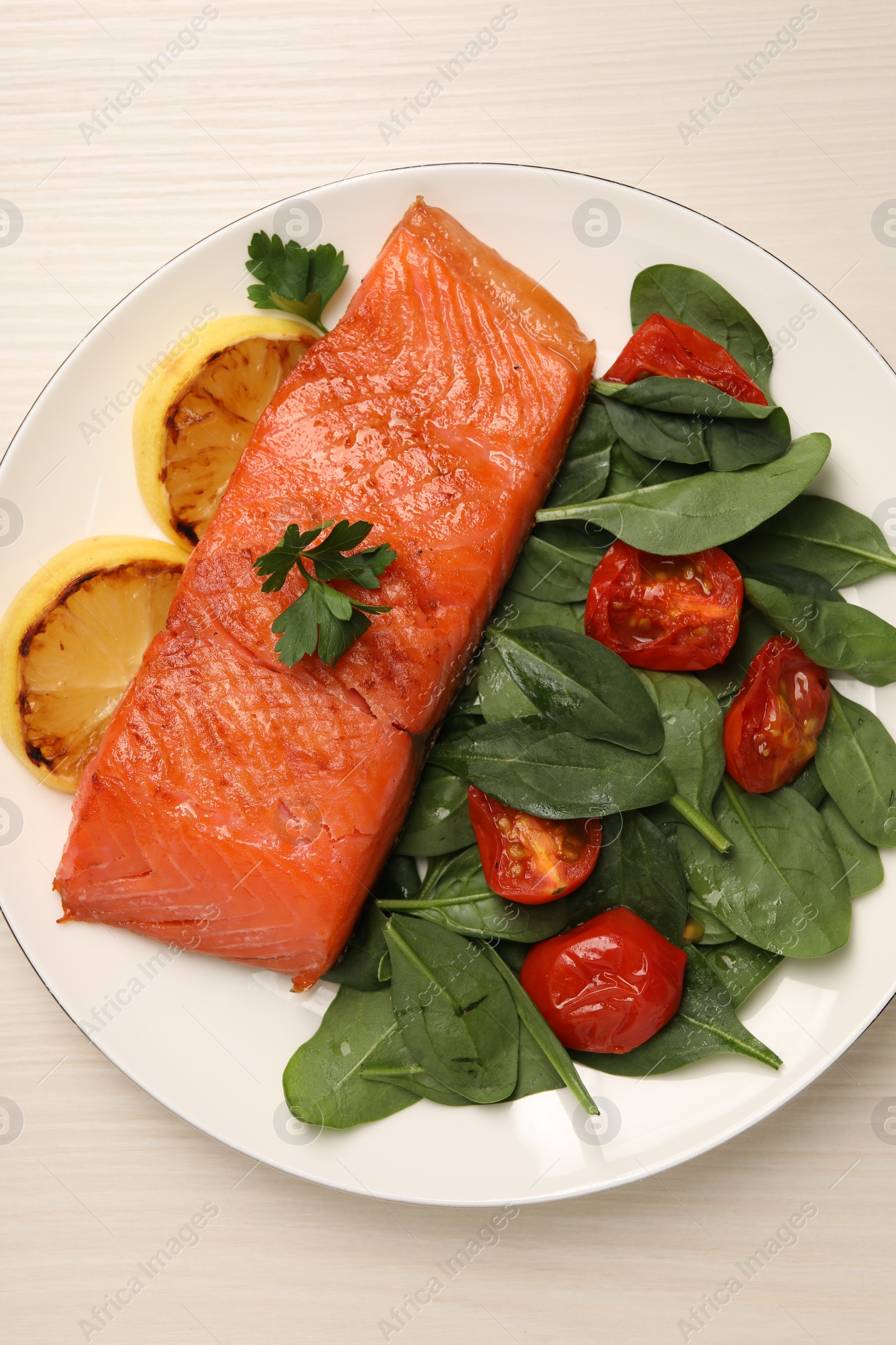 Photo of Tasty grilled salmon with basil, tomatoes and lemon on white wooden table, top view