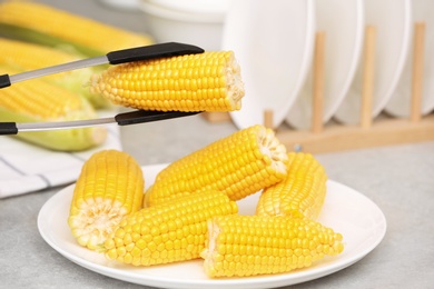 Photo of Taking corn cob from plate with tongs, closeup