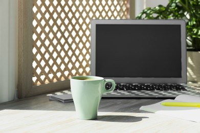 Cup of coffee, laptop with blank screen, stationery on wooden window sill. Space for text