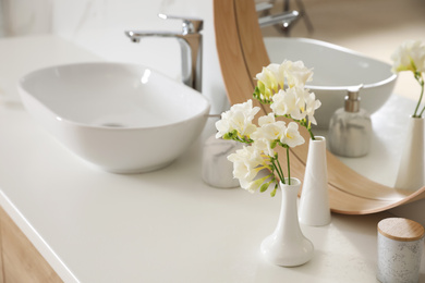 Photo of Beautiful white freesia flowers on countertop in bathroom, space for text