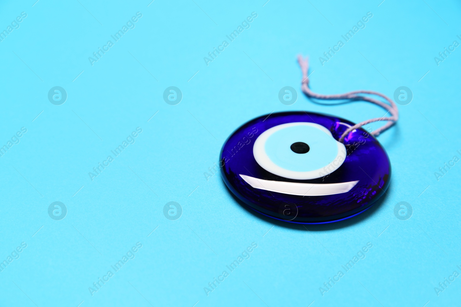 Photo of Evil eye amulet on light blue background. Space for text