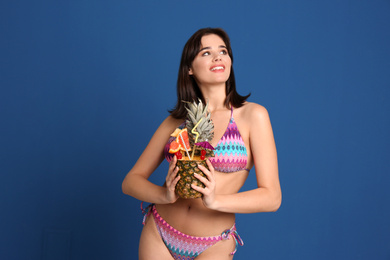 Beautiful young woman with exotic cocktail wearing bikini on blue background