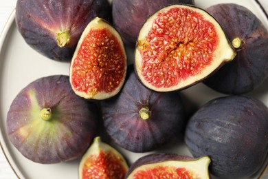Photo of Plate with whole and cut ripe figs on table, top view